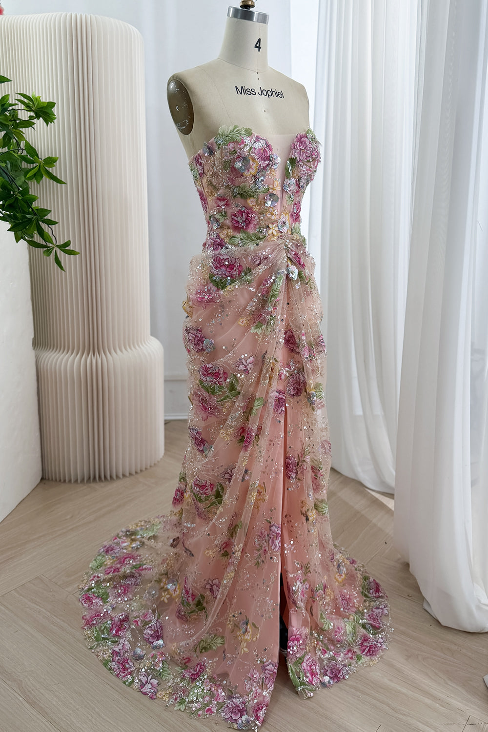 Angled portrait peach flower formal evening attire reveals ruched hip gather, shimmering layered skirt, occasion styling fit.