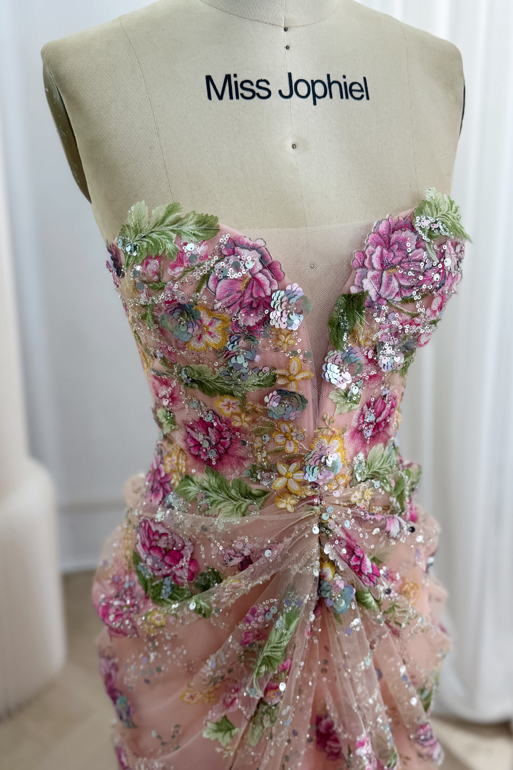 Closeup pink floral corset gown showing sparkling sequins, strapless neckline, sheer embroidery, mannequin studio scene shot.