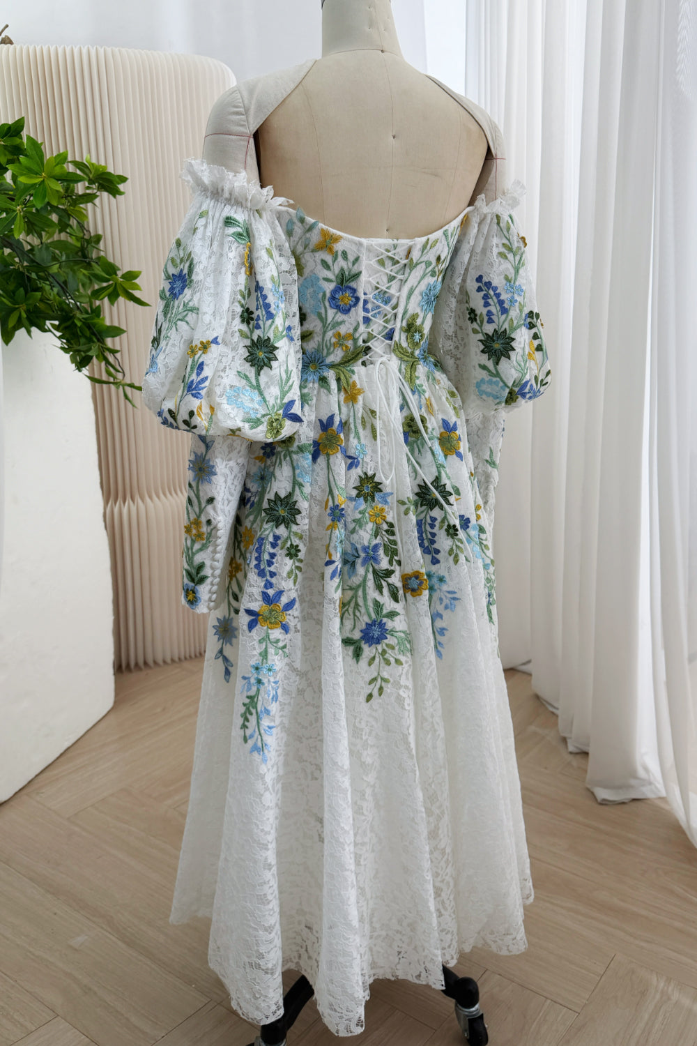 Rear perspective: ivory botanical midi frock, crossback ties, gathered skirt, Bardot balloon arms, ceremony fashion aesthetic