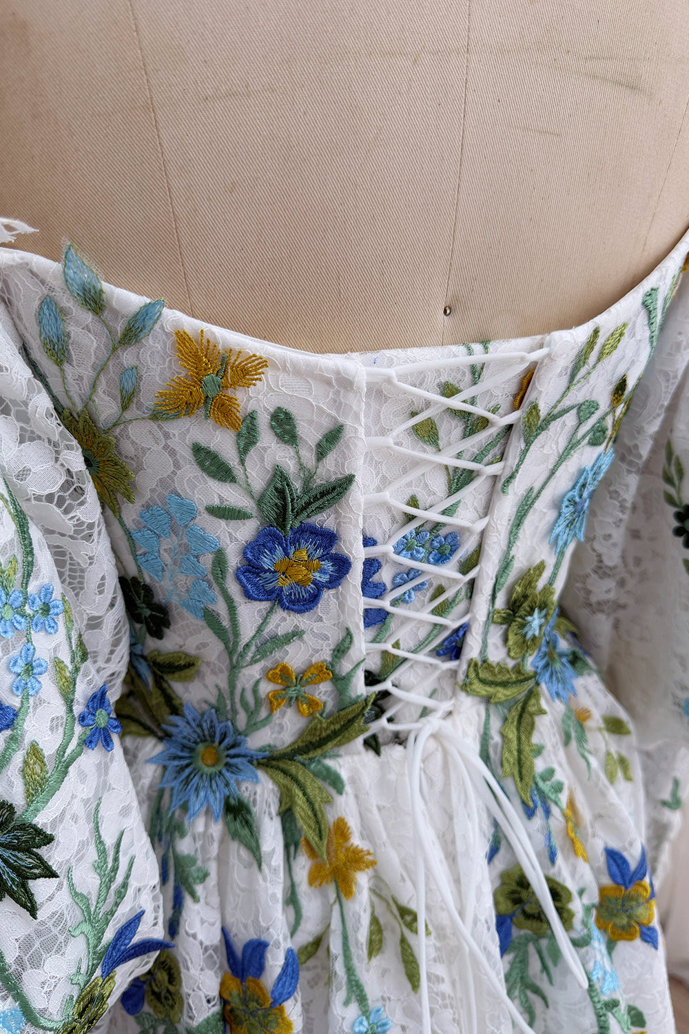 Closeup captures crisscross fastening, blue floral needlework, fitted bodice panels, artisanal bridal craftsmanship detailing