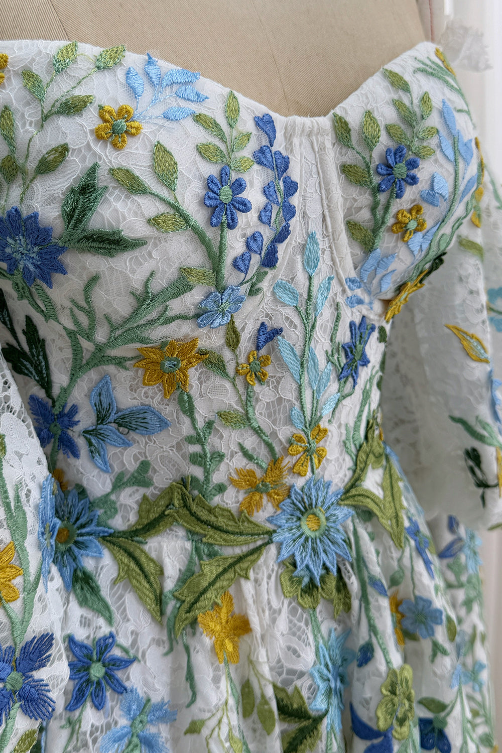 Macro detail highlights delicate mesh overlay, green vines, yellow daisies, dimensional stitching, whimsical texture richness