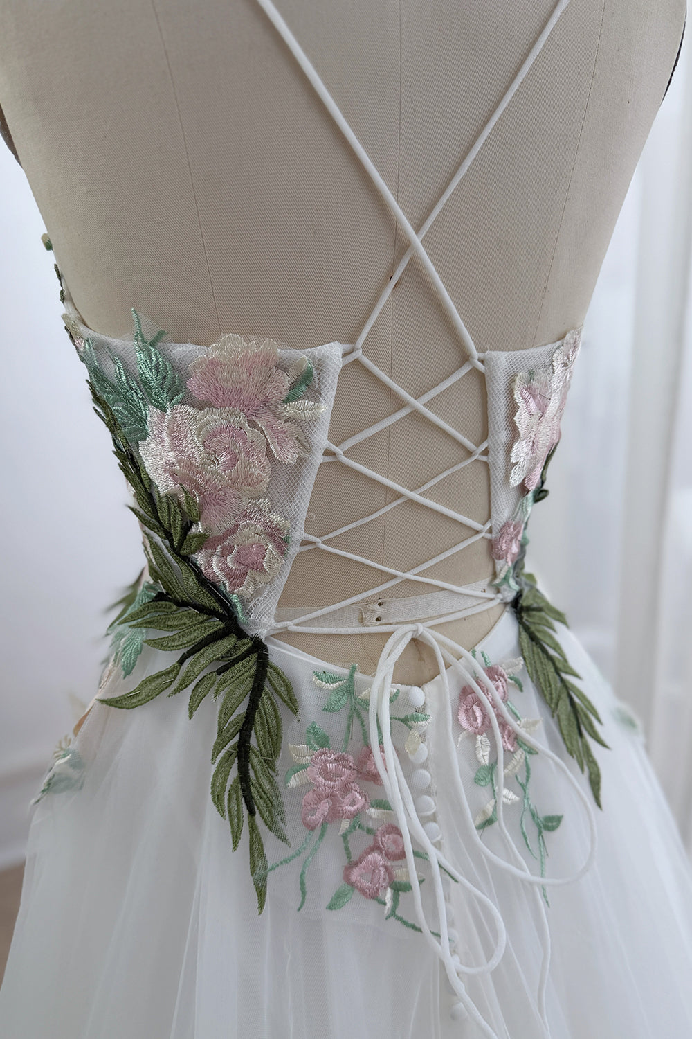 Rear corset view shows crossed spaghetti straps, open back, pastel roses, leafy appliques, fitted waist, plus covered buttons