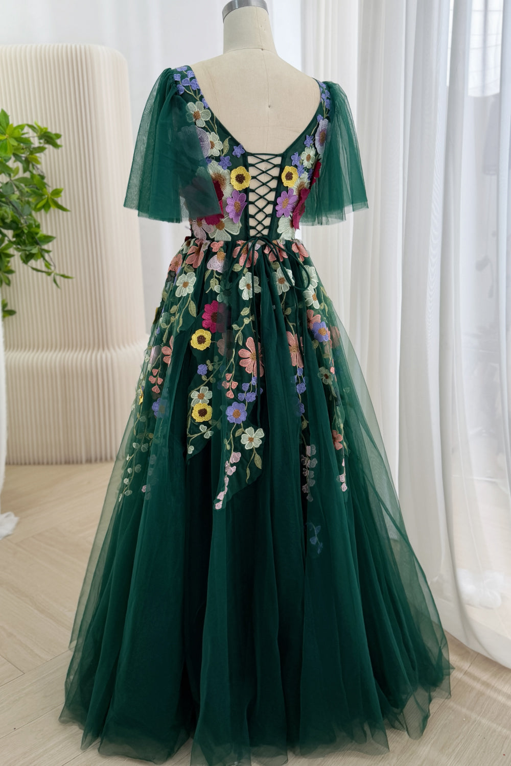 Rear portrait shows forest lace-up corset, multicolor blossoms, sheer capelets, sweeping floor-length skirt, romantic profile