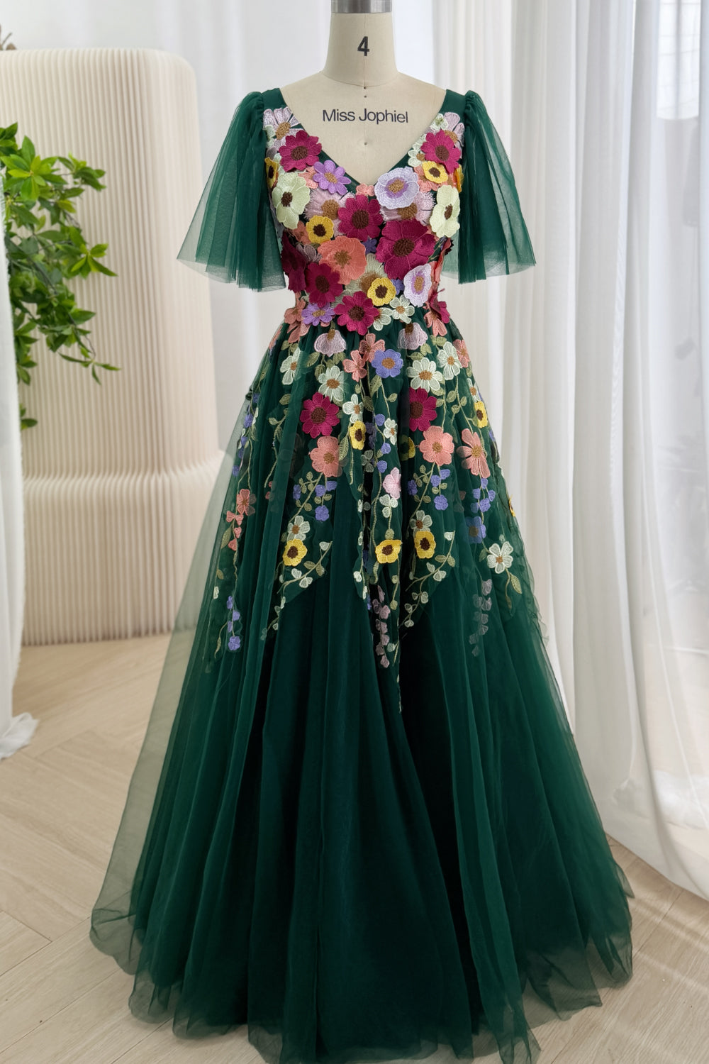 Full-length studio shot displays deep-green floral gown, fitted top, cinched waistline, voluminous layers, prom-ready glamour