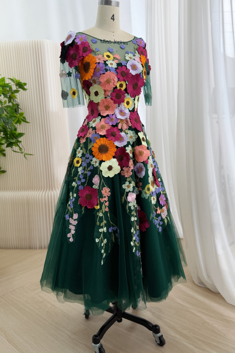 Oblique angle reveals jewel-toned occasion frock with fitted waist, layered mesh silhouette, vivid daisies, romantic fullness