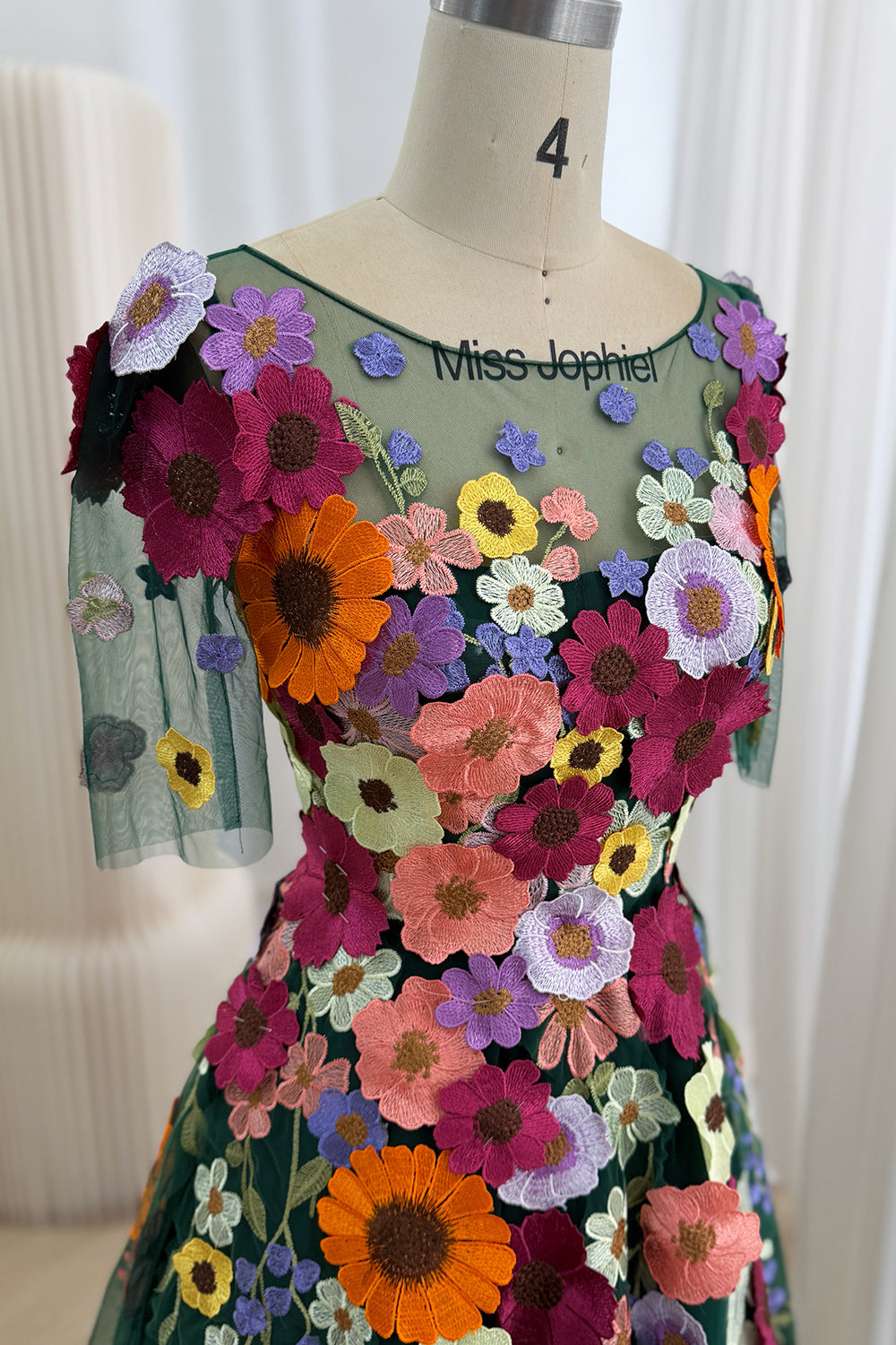 Side portrait captures dark green partywear, dainty short arms, rich gerbera embroidery, defined midsection, formal elegance.