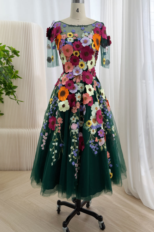 Emerald embroidered tea-length dress on mannequin, bearing sheer bateau neckline, elbow sleeves, colorful flora, A-line skirt