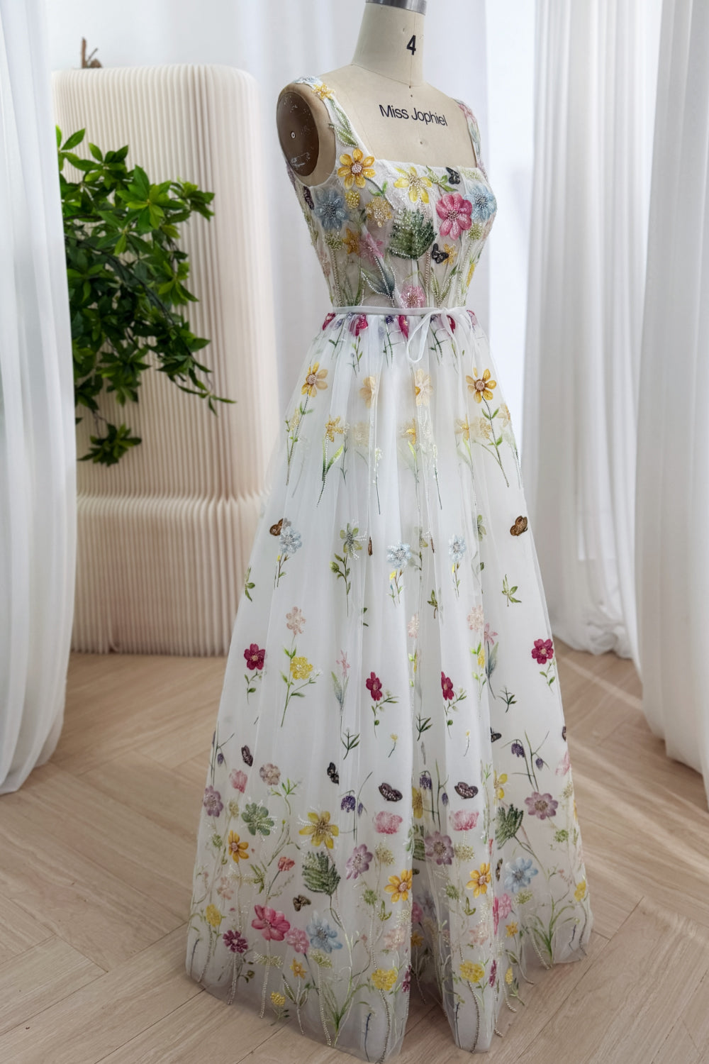 Angled portrait highlights sparkling sequins, vibrant appliqués, sculpted waist, flowing silhouette, plus botanical artistry.