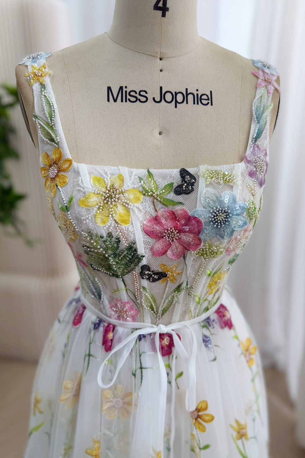 Macro bodice photograph reveals yellow, blush, azure petals, pearl accents, butterfly motifs, structured panels beneath mesh.