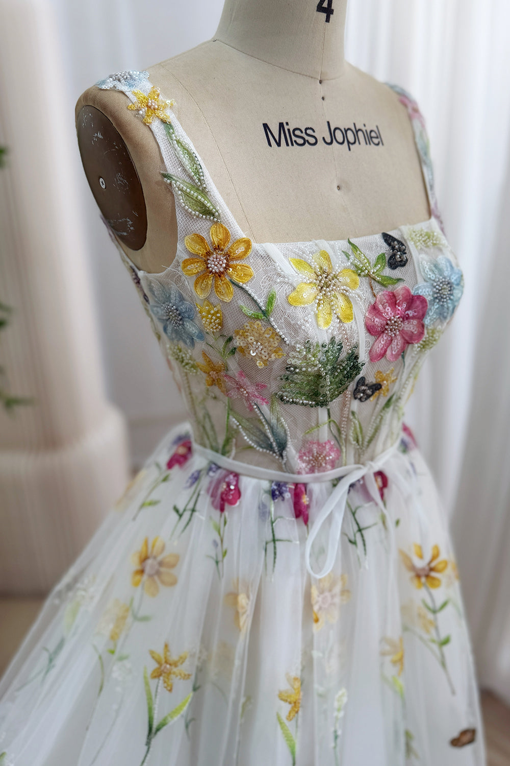Closeup showcases multicolor beadwork, blossoms, leafy embroidery, transparent boned corsetry across the ivory tulle overlay.