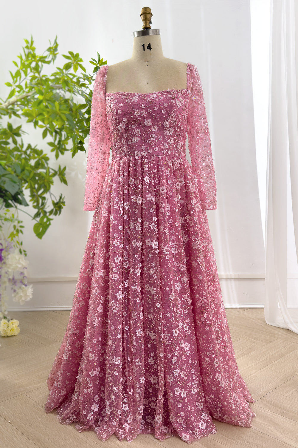 Radiant square neck rose gown shimmering sequins adorning sheer sleeves displayed elegantly on mannequin in bright studio setting