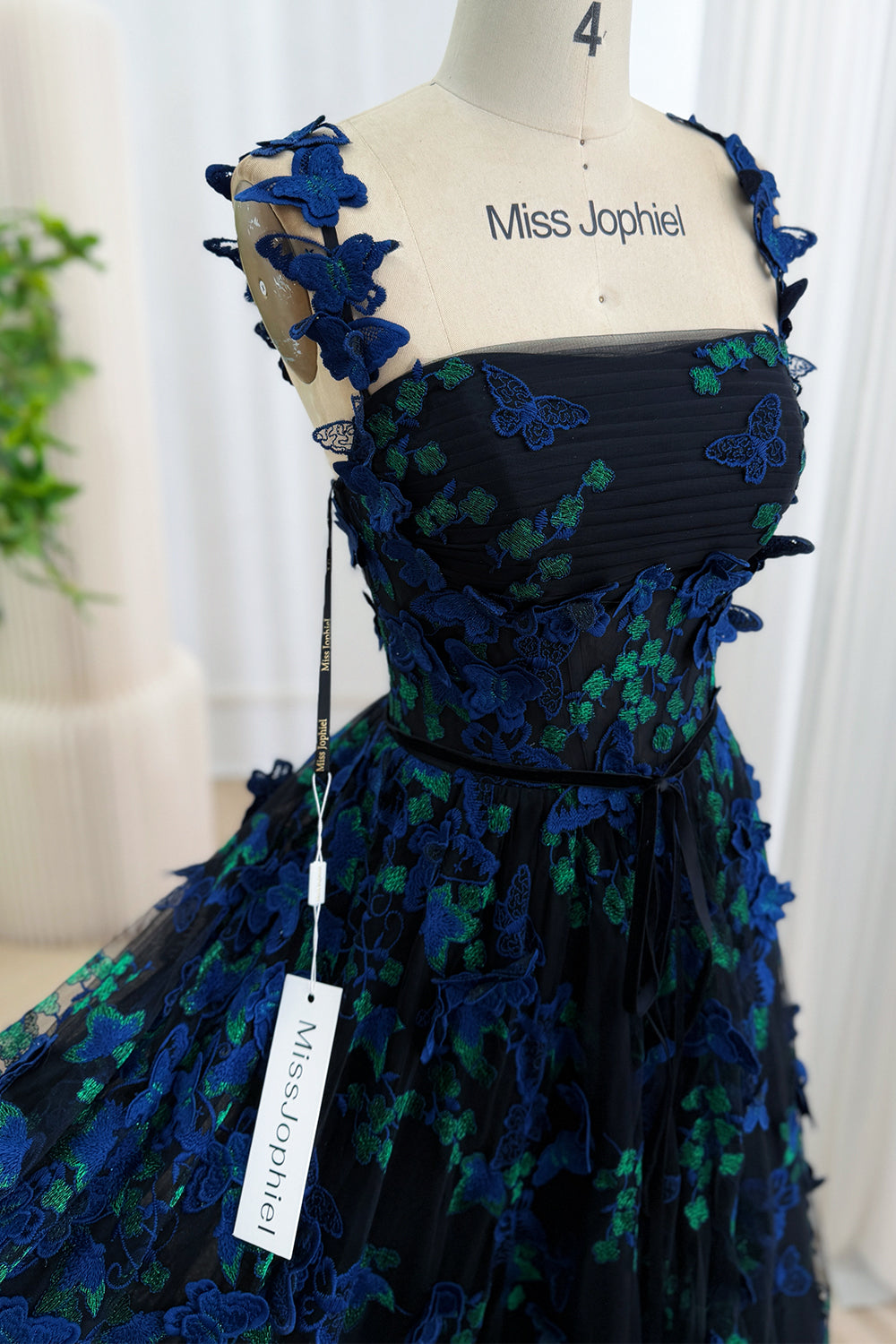 Close-up of the straight neckline bodice of a black gown with royal blue and emerald 3D butterfly appliqués and sheer butterfly straps