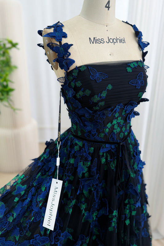 Close-up of the straight neckline bodice of a black gown with royal blue and emerald 3D butterfly appliqués and sheer butterfly straps