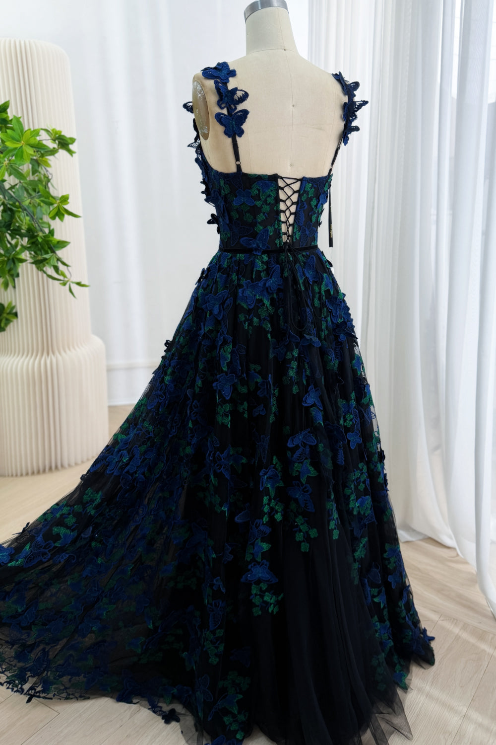 Back view of a black A-line gown showing the lace-up corset closure and butterfly appliqué tulle skirt