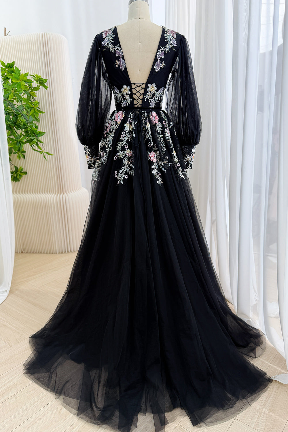 Back view of a black tulle formal gown showing a deep V-back with corset lace-up detail and floral sequin embroidery
