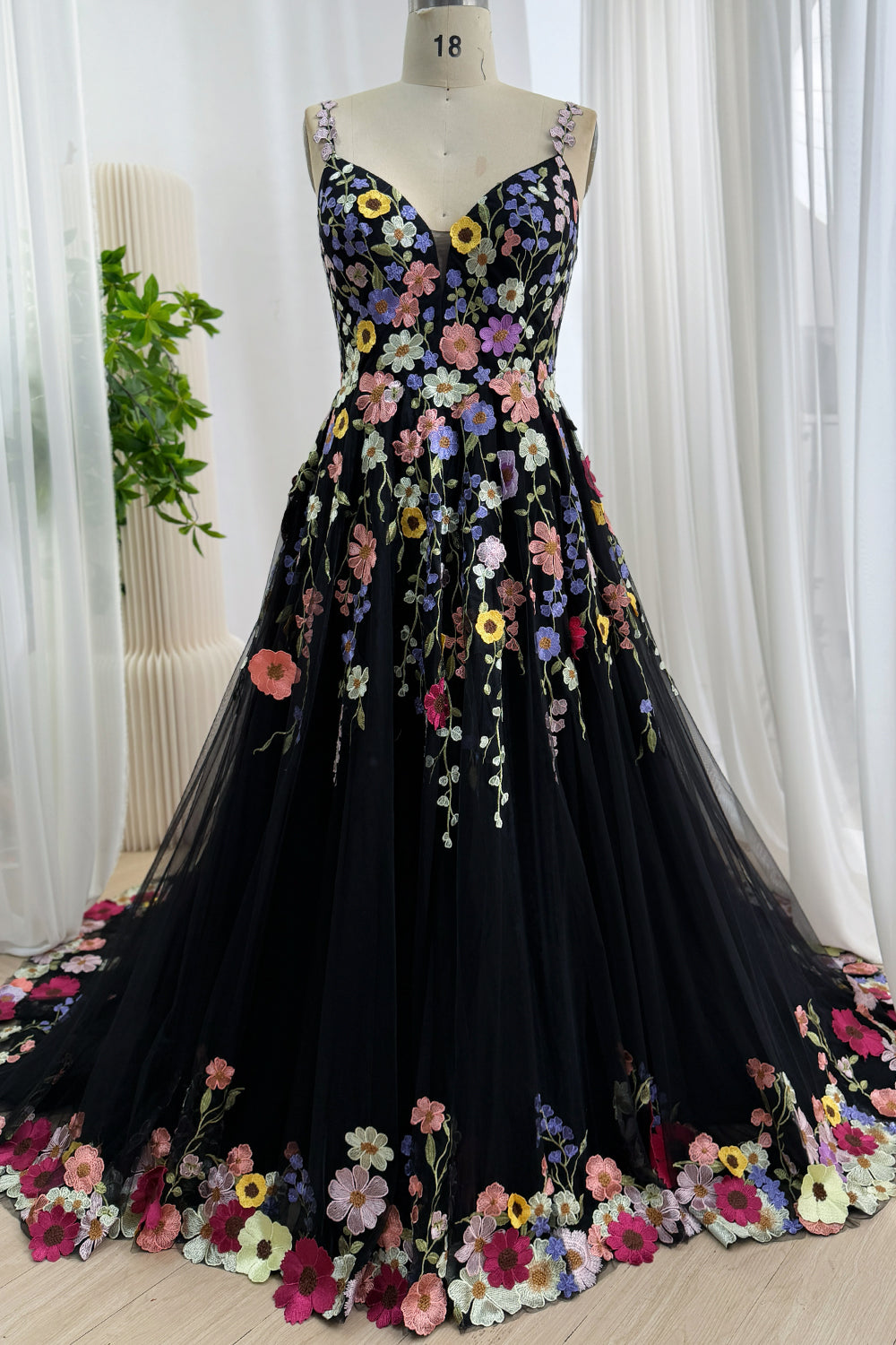 Front view of a black A-line tulle prom dress with colorful floral embroidery displayed on a mannequin.