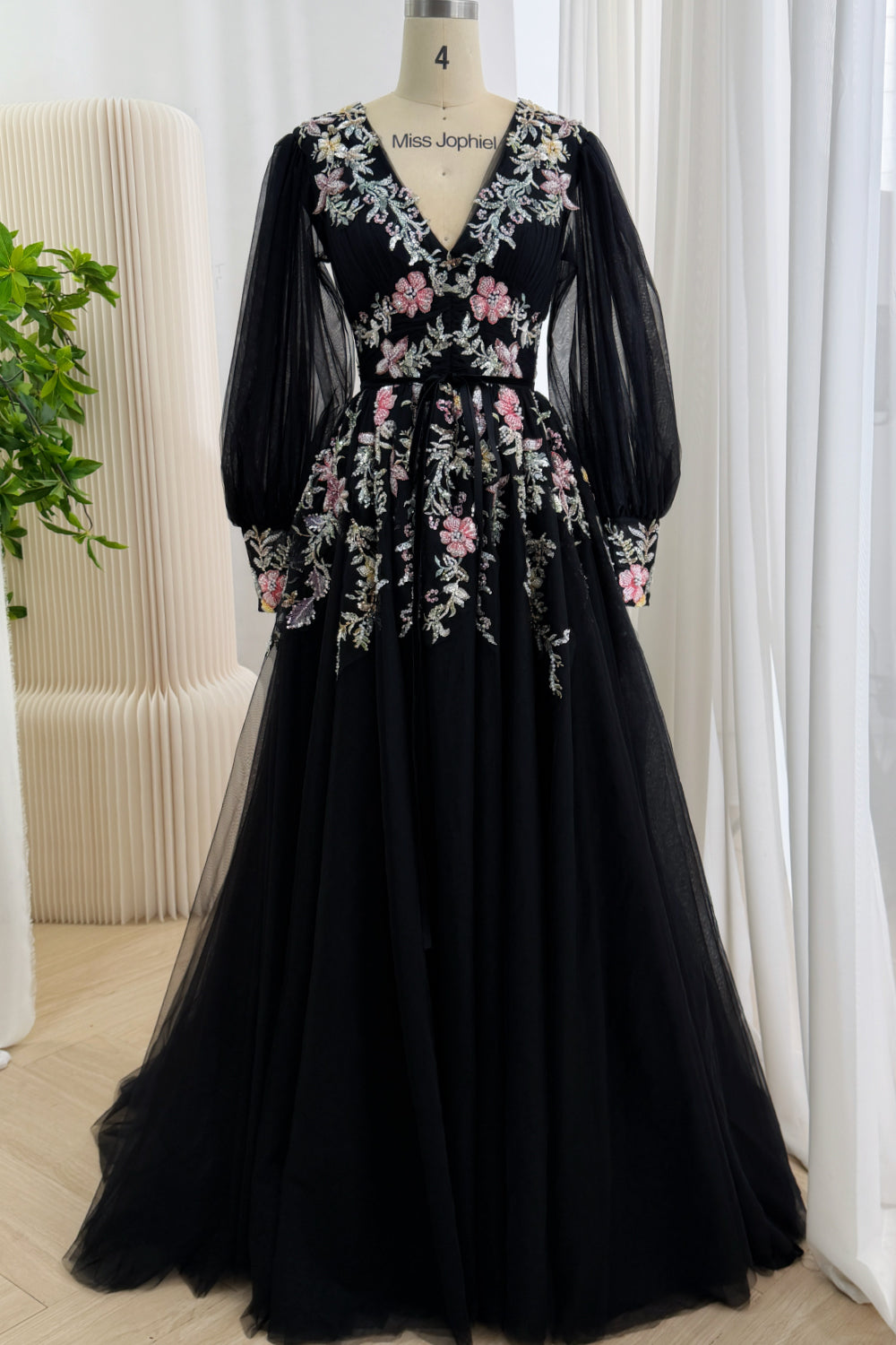 Front view of a black A-line evening gown with a plunging V-neck, sheer bishop sleeves, and pink and silver sequin floral embroidery on a mannequin