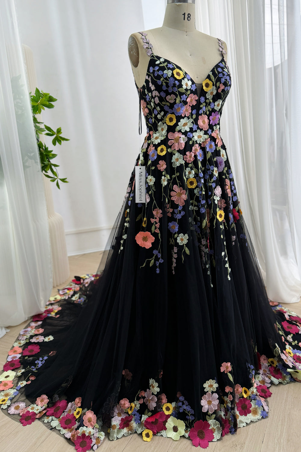 Angled front view of a black floral embroidered tulle formal gown showing the sweeping train on a mannequin.