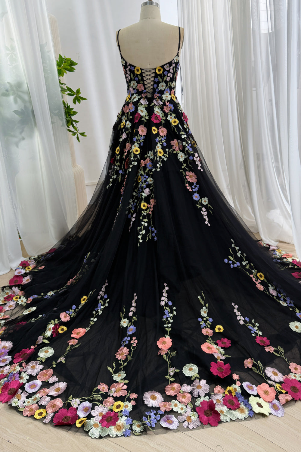 Back view of a black floral embroidered tulle dress on a mannequin highlighting the sweeping train and corset back.