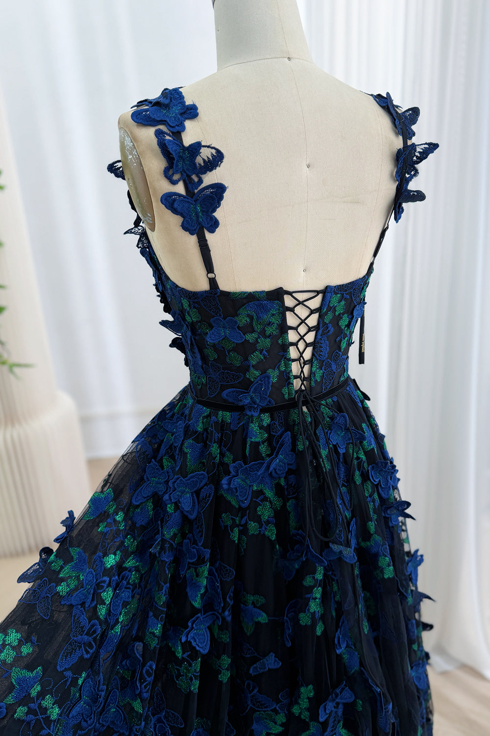 Close-up of the lace-up corset back and sheer butterfly appliqué shoulder straps on a black evening gown