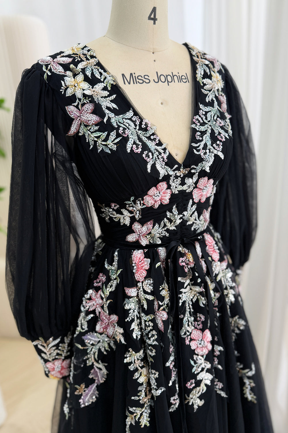 Close-up of the pleated V-neck bodice, sheer bishop sleeves, and pink floral sequin embroidery with a self-tie waist sash