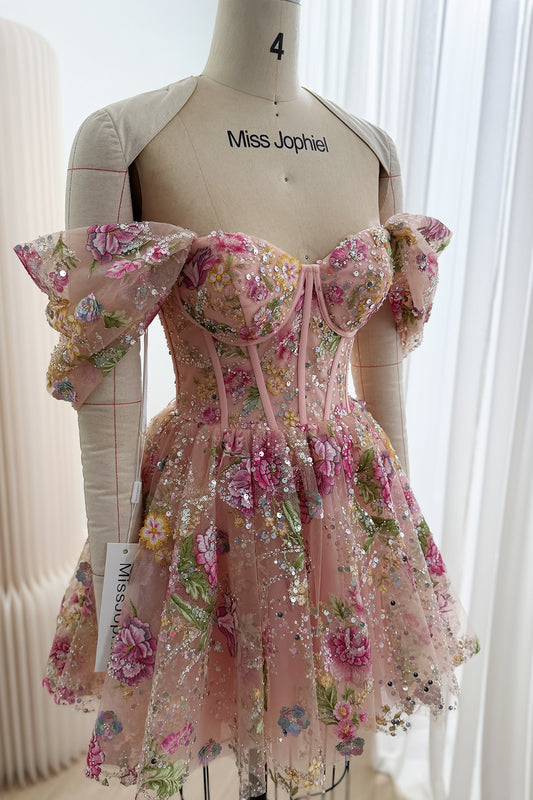 Angled front view of a blush pink embroidered tulle mini dress showing draped off-the-shoulder sleeves and a fitted corset bodice.