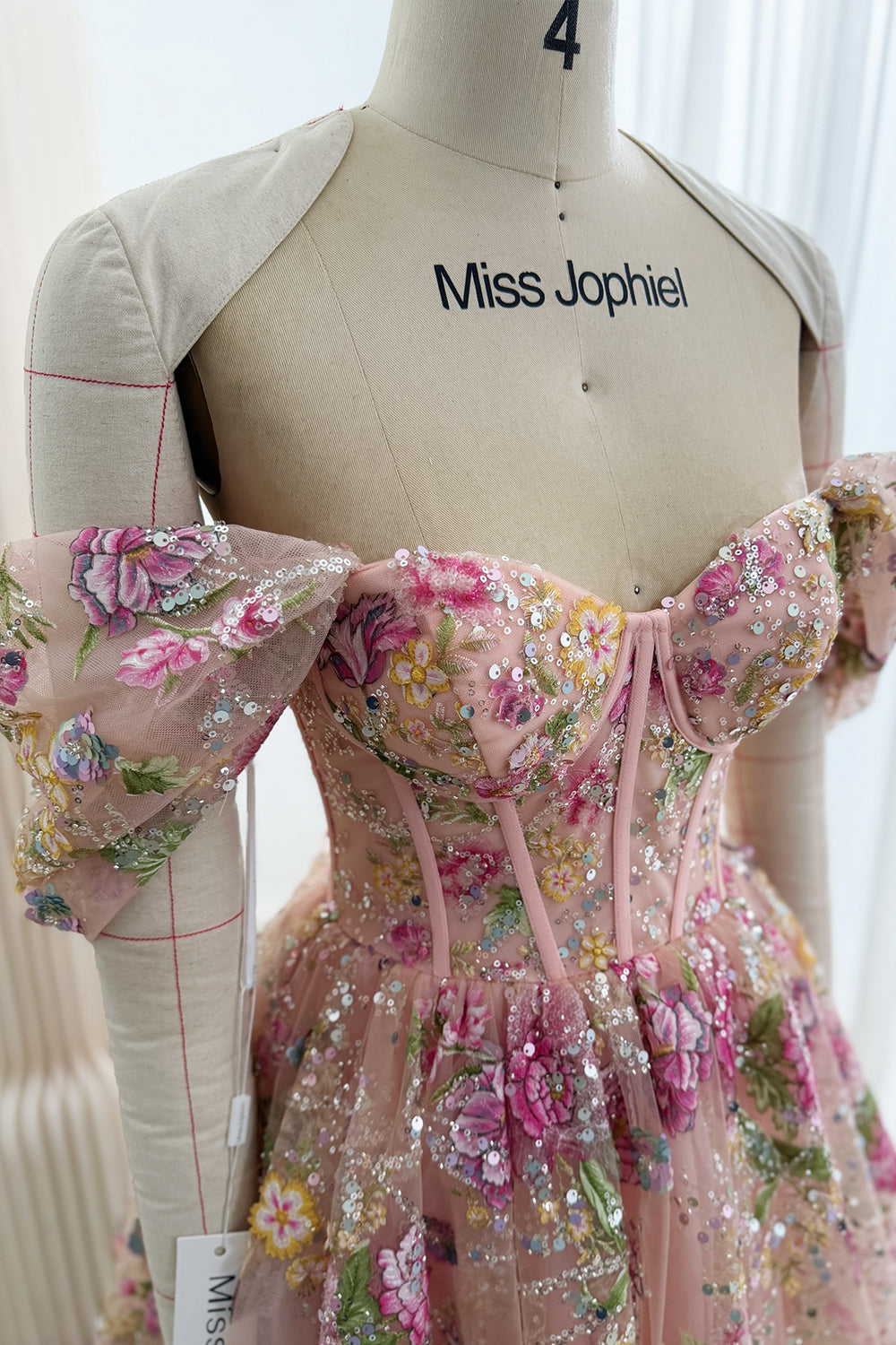 Close-up of the sweetheart corset bodice and draped sleeve, with pink floral embroidery and reflective sequins on blush tulle.