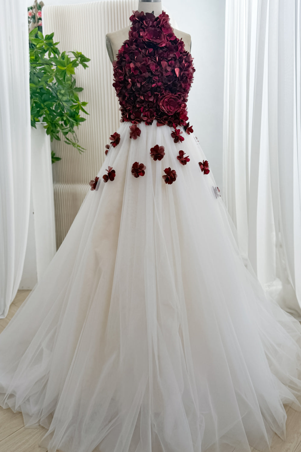 Front view of burgundy 3D floral halter ball gown with ivory tulle skirt on mannequin