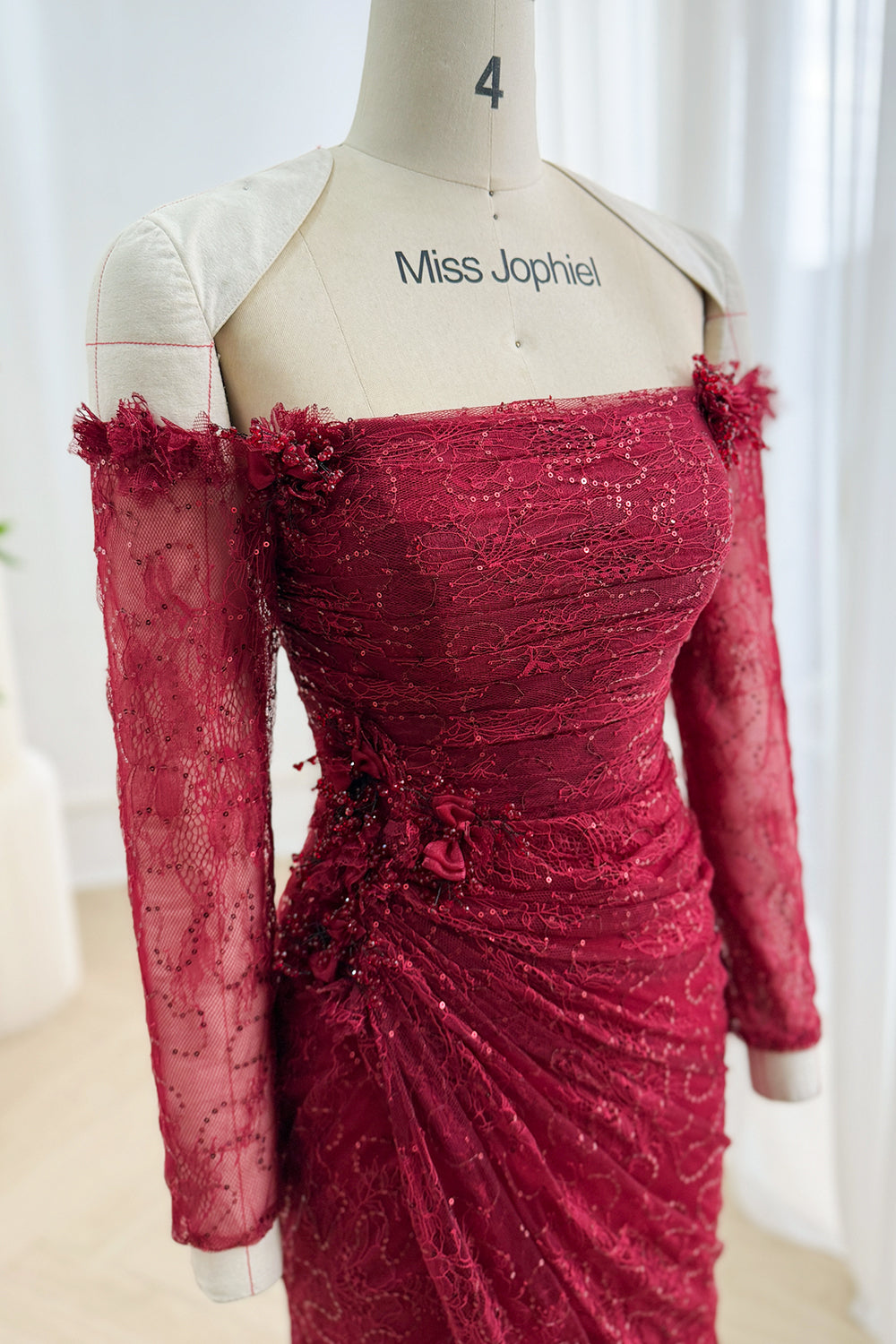 Close-up of burgundy floral lace gown with straight neckline, sequins, appliqués, and ruched waist