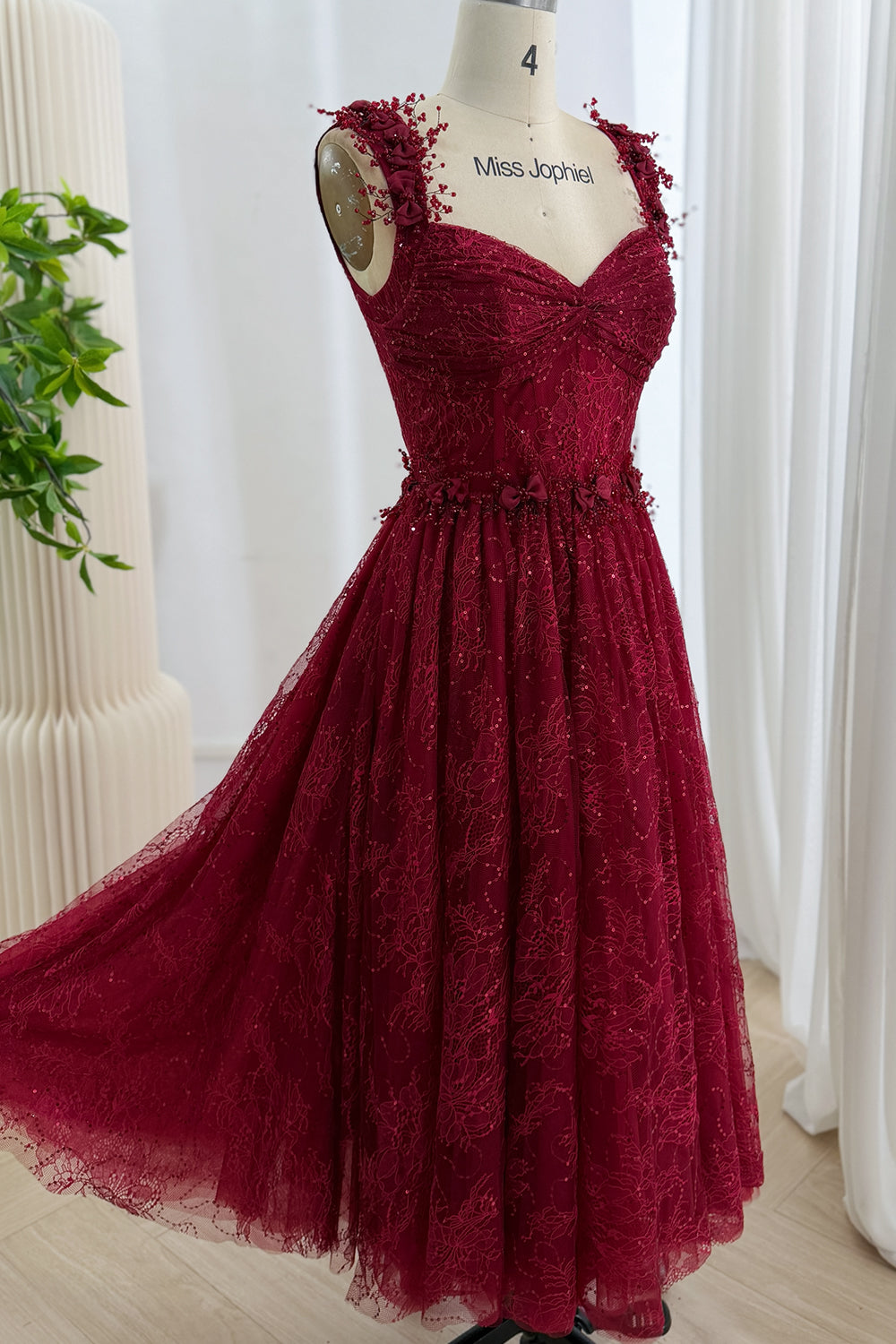 Front view of a burgundy sequin lace tea-length A-line dress with floral shoulder straps
