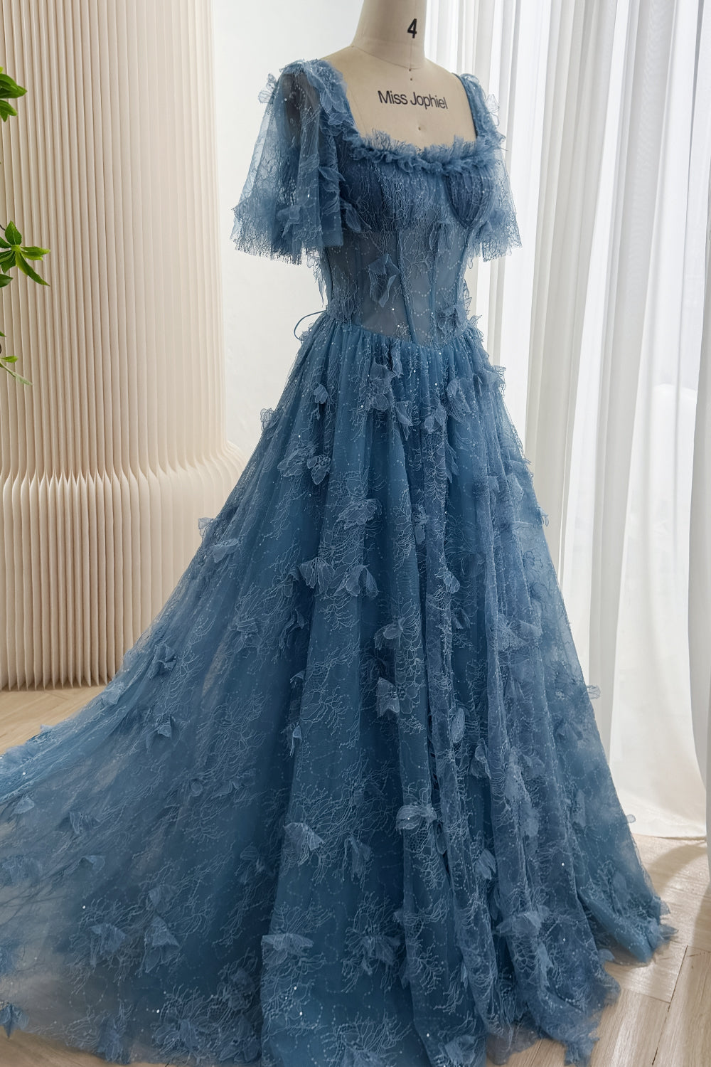 Angled full-length view of dusty blue A-line floral lace gown with short flutter sleeves, scattered sequins, and a flowing train.
