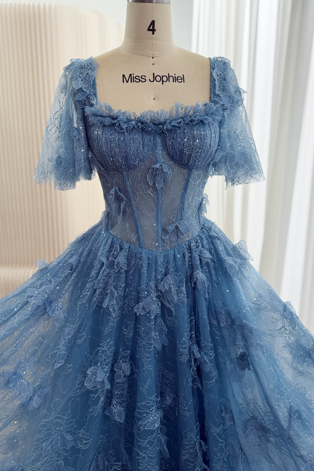 Front bodice detail of dusty blue gown with defined cups, visible corset boning, sheer waist panels, and floral lace.