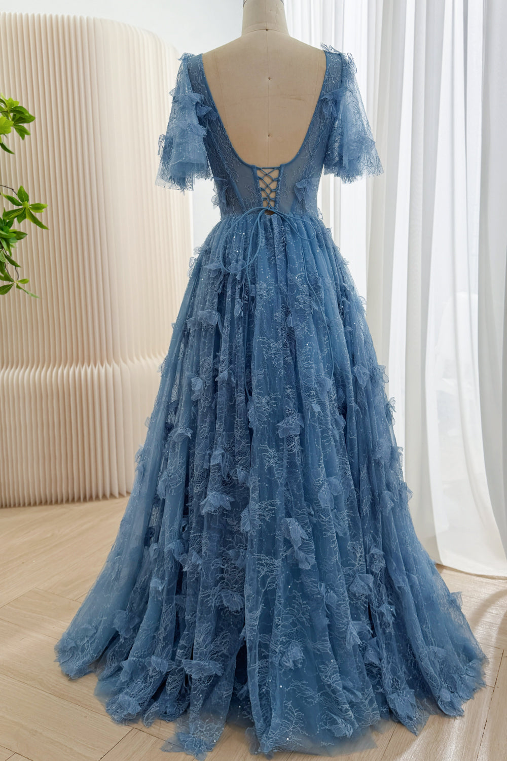 Full back view of dusty blue floral lace gown with a low scoop back, corset lacing, flutter sleeves, and trailing skirt.