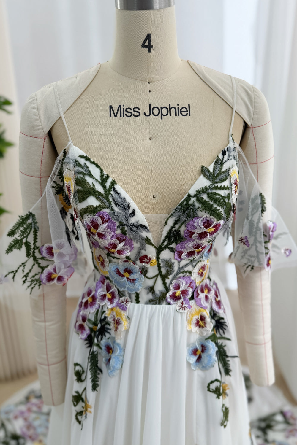 Front bodice detail showing spaghetti straps, a deep V-neckline, dimensional pansy embroidery, and draped tulle panels