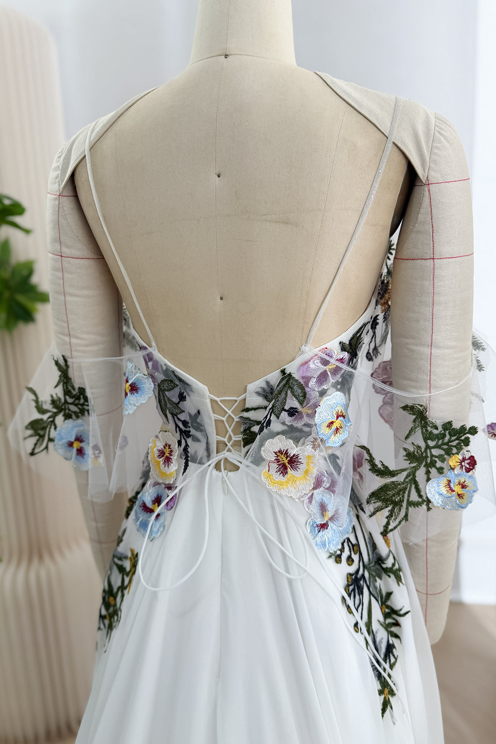 Close-up of the gown's low open back with thin straps, corset-style lacing, and embroidered sheer tulle