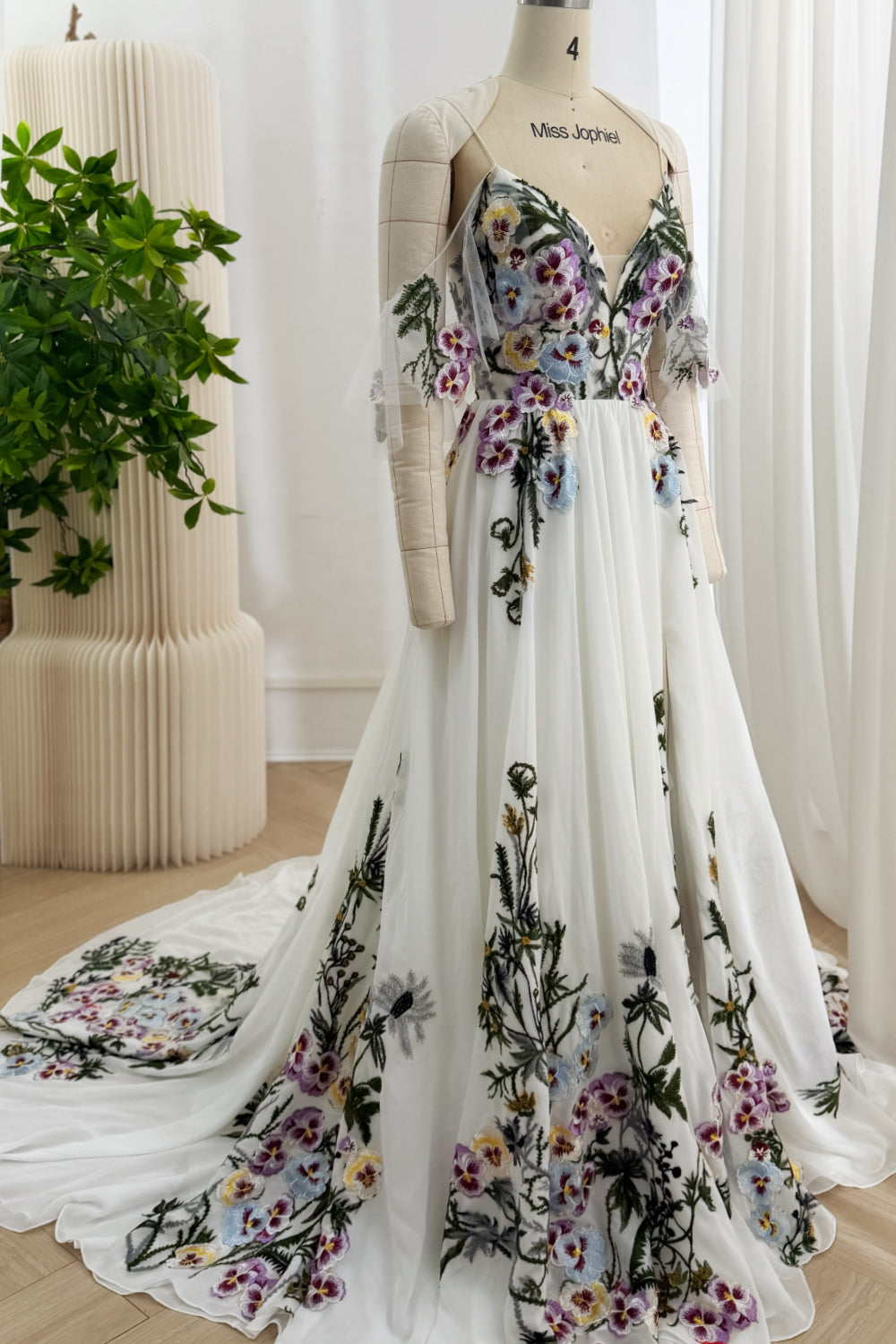 Front view of an ivory A-line gown with a deep V-neck bodice, multicolor floral embroidery, and a flowing train