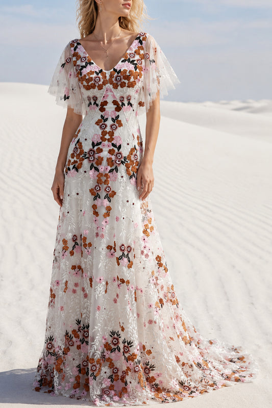 Model wearing an ivory multicolor floral embroidered floor-length gown in a white desert setting