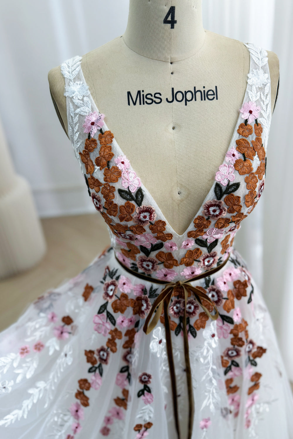 Close-up of the ivory tulle bodice with a plunging V-neck, colorful floral embroidery, and brown ribbon waist tie