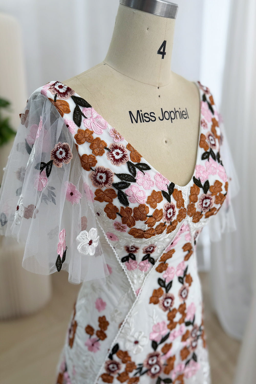 Detail of pink, rust, burgundy, white, and dark floral embroidery on the ivory tulle bodice and sleeve