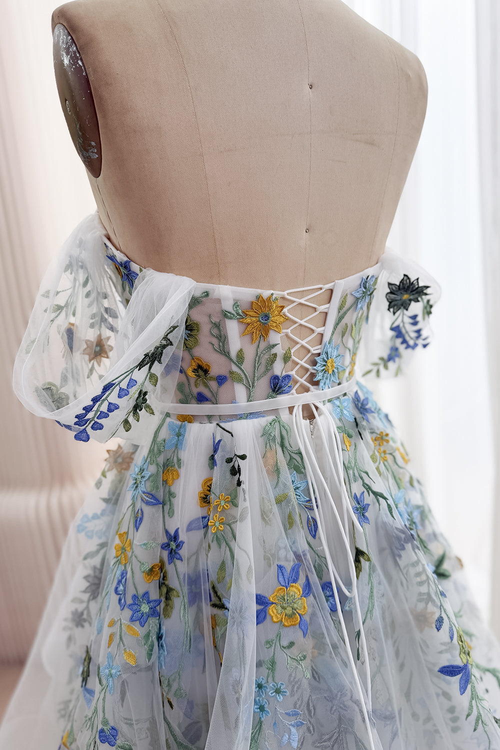 Rear bodice detail of the ivory floral tulle gown showing crisscross lacing, embroidered flutter sleeves, and a narrow ribbon waist tie.