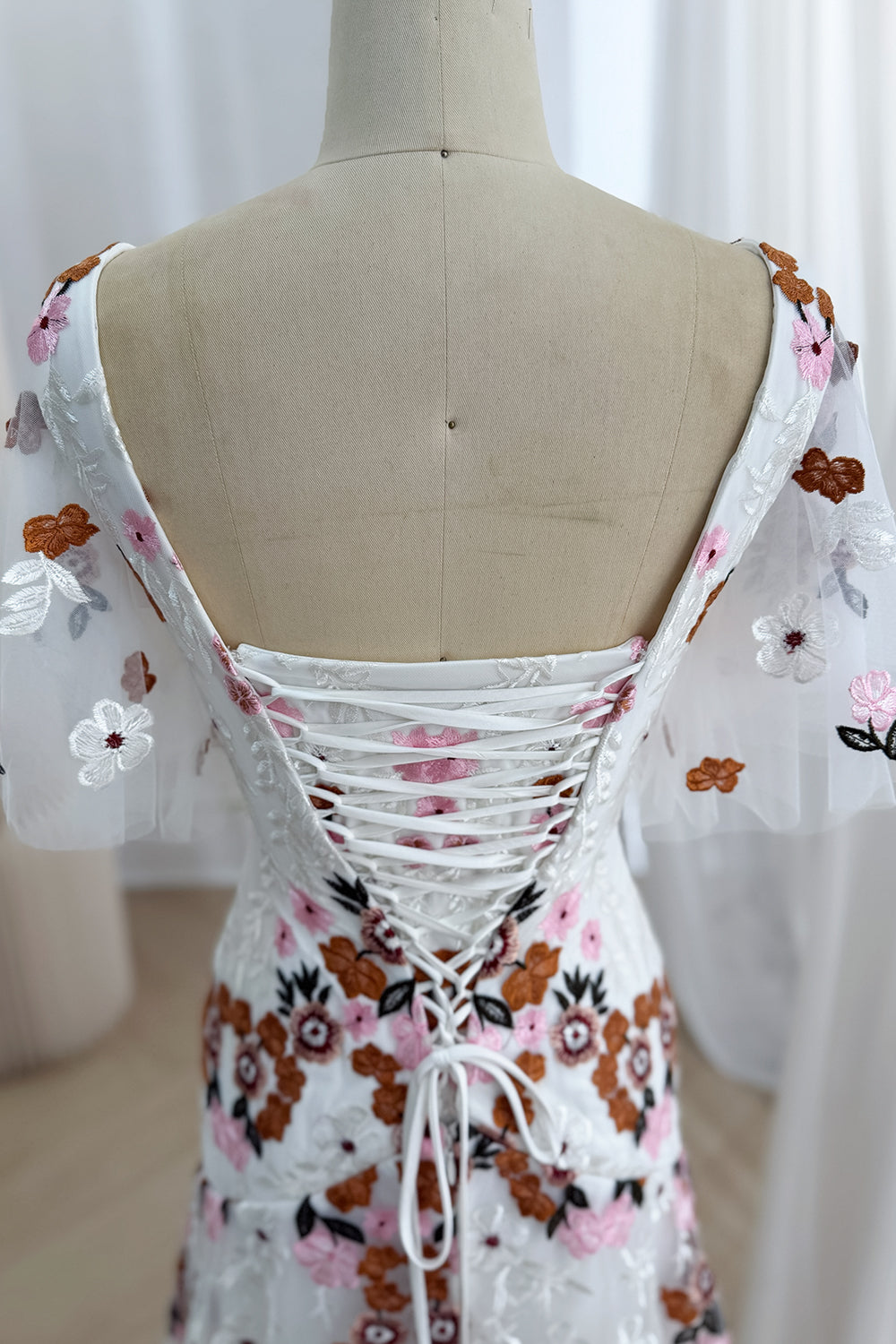 Close-up back view of the ivory embroidered gown showing its low lace-up corset closure