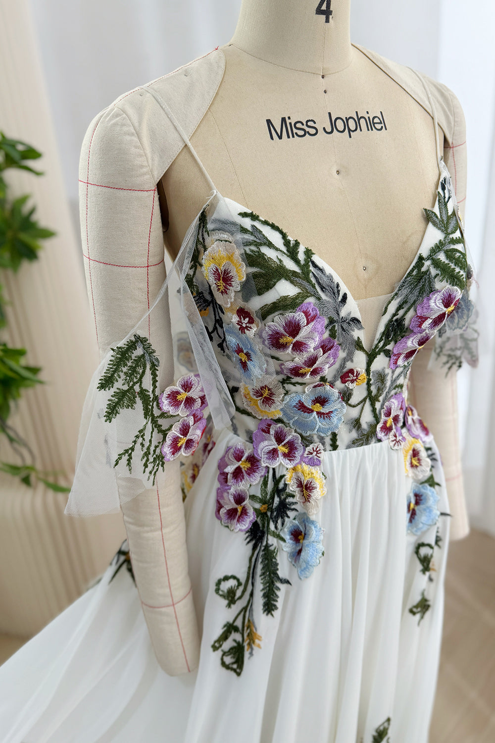 Close-up of the deep V-neck bodice with purple, blue, yellow, and green floral embroidery and sheer tulle panels