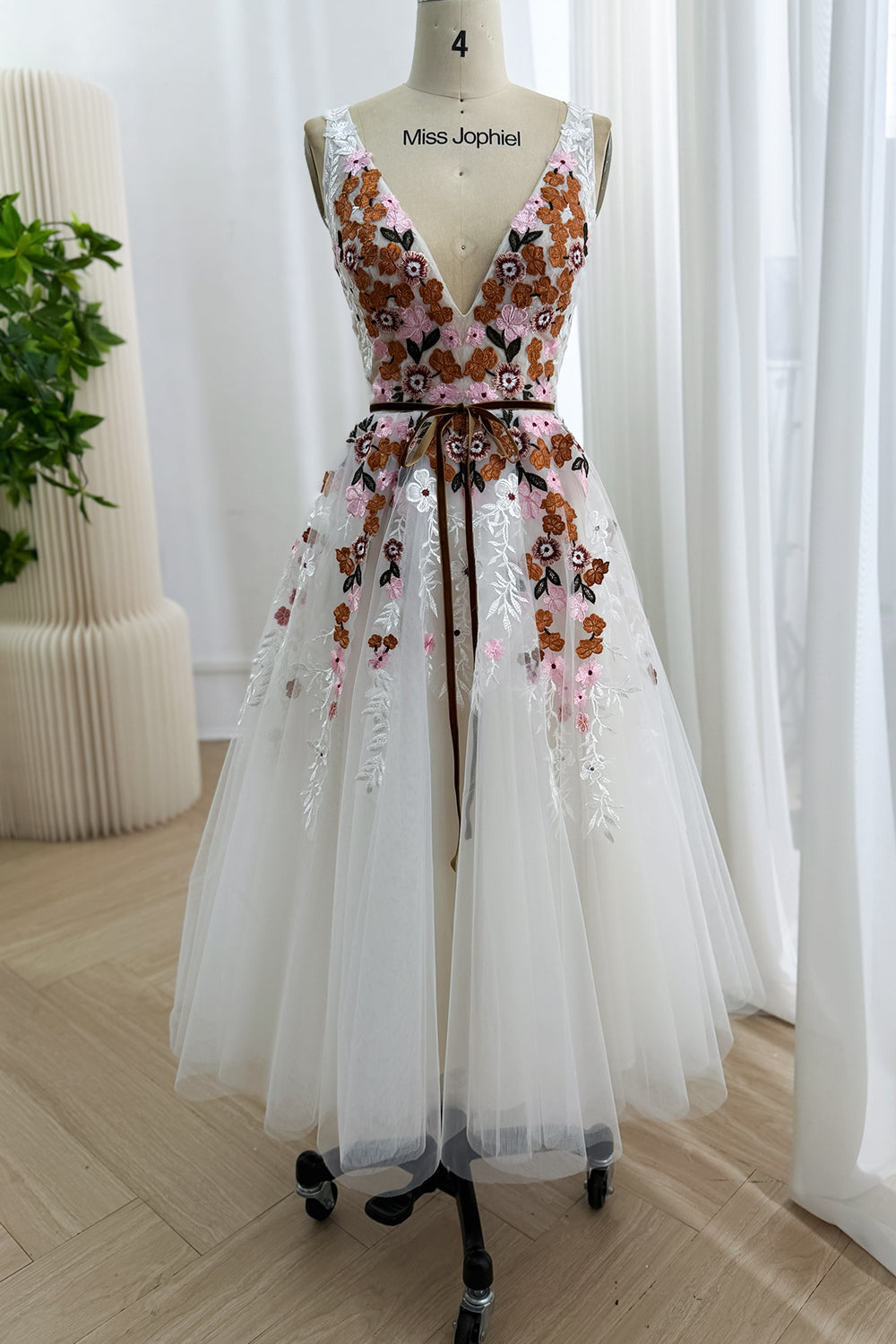 Front view of the ivory tea-length A-line dress with colorful floral embroidery and a plunging V-neckline