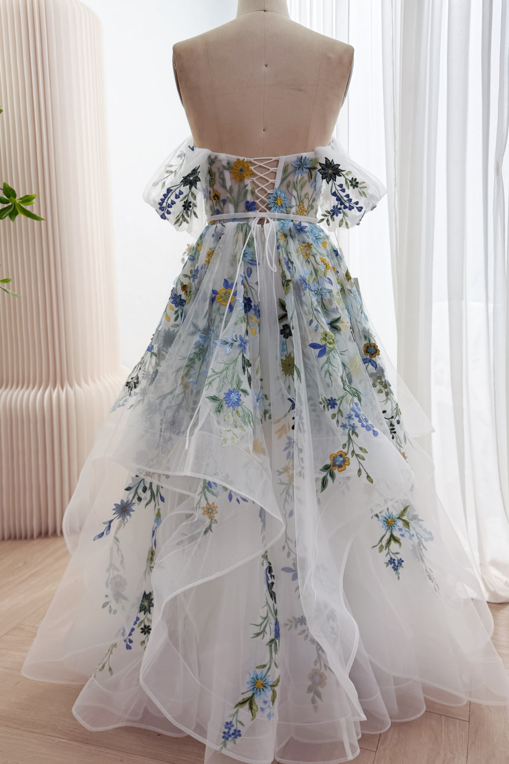 Back view of the ivory wildflower embroidered gown with a lace-up bodice, ribbon waist tie, and layered cascading tulle skirt.