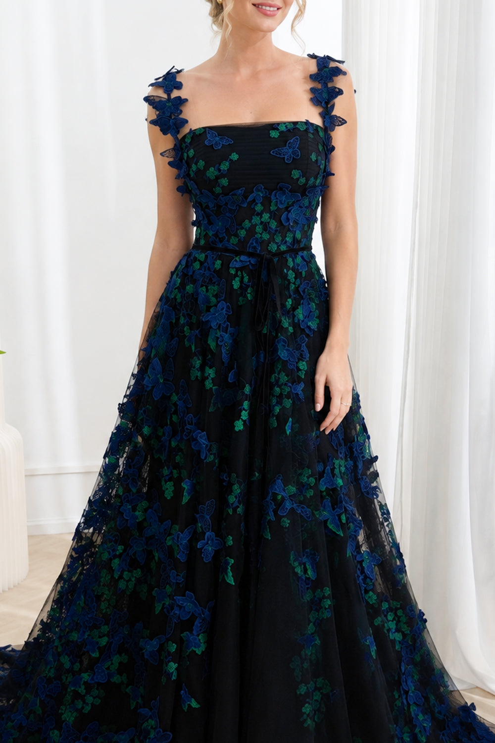 Model wearing a black floor-length A-line prom dress with royal blue and emerald 3D butterfly appliqués