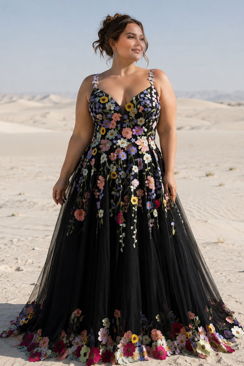Plus size model posing in a desert wearing a black floral embroidered V-neck tulle prom dress.
