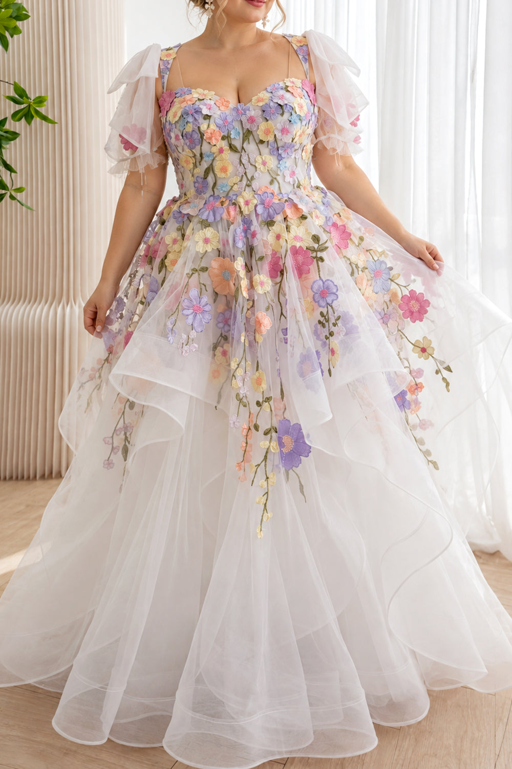 Model wearing a white pastel floral wedding dress with a sweetheart bodice, bow-trimmed puff sleeves, and a full cascading ruffle skirt.