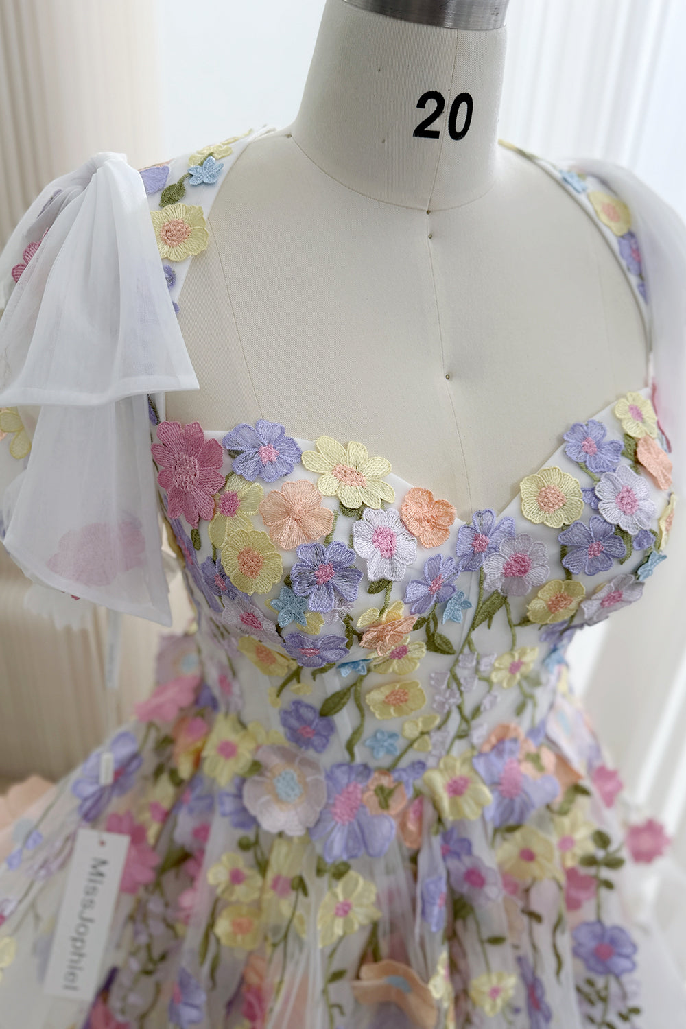 Close-up of the sweetheart bodice with pink, lavender, yellow, and peach embroidered flower appliqués and a sheer white shoulder bow.