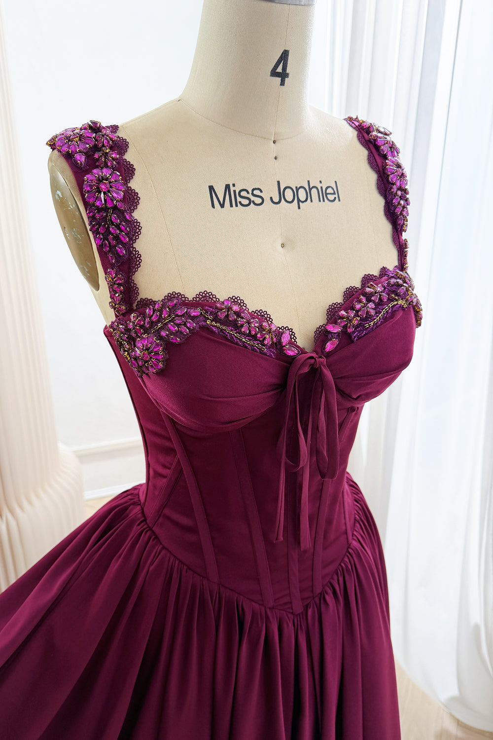 Close-up of plum corset dress with sparkling floral straps, lace-edged sweetheart neckline, gathered bust, and front bow.