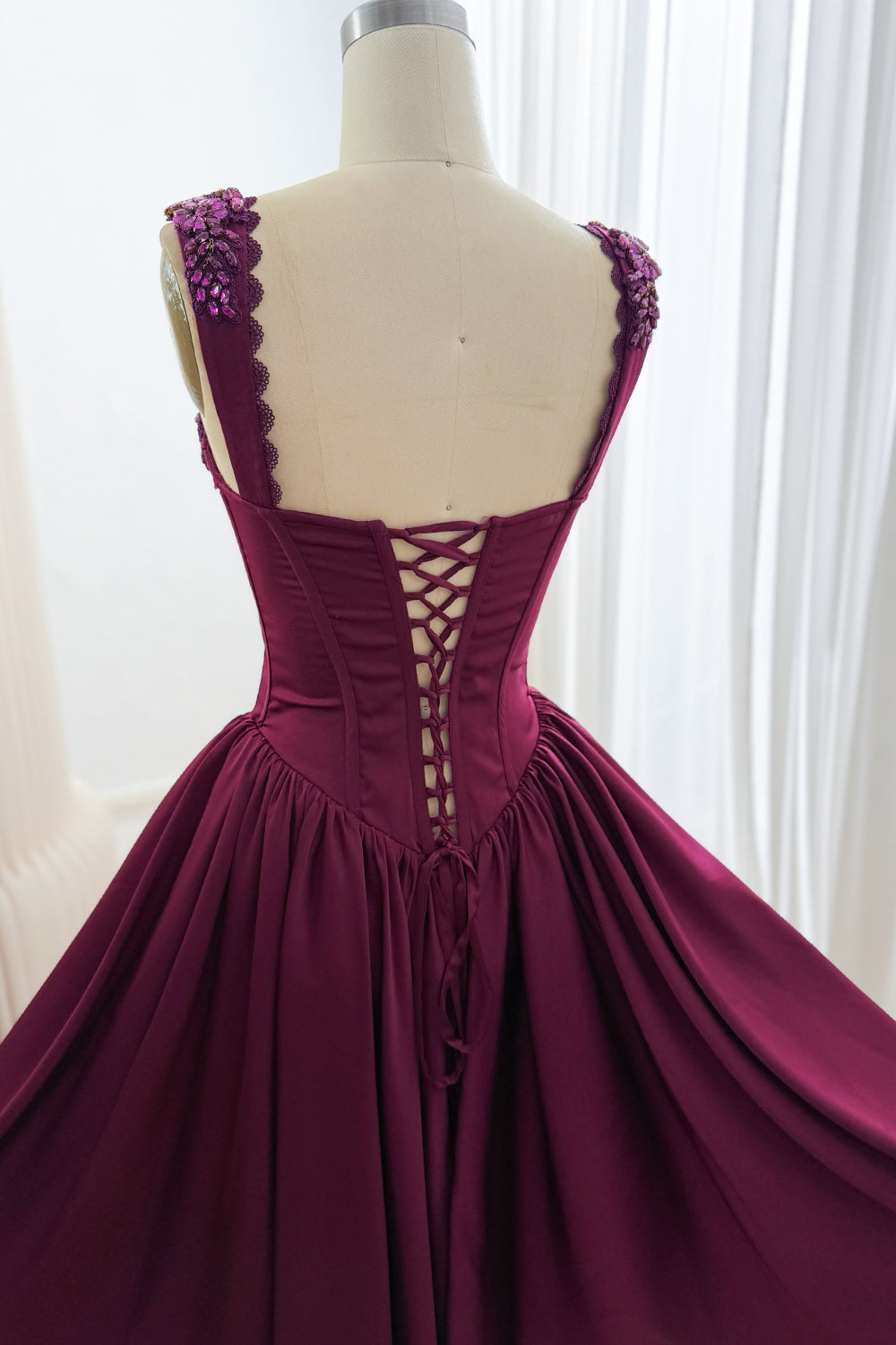 Back detail of plum dress showing corset lacing, embellished wide straps, pointed waist, and gathered skirt.